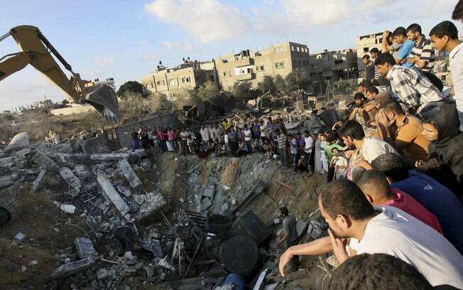 Palestinos se reúnem ao redor de escombros de prédio onde membros de uma mesma família foram mortos em ataque de Israel em Khan Younis (26/7)