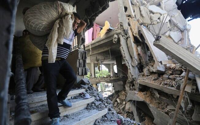 Palestinos carregam seus pertences em uma casa depois de ela ser destruída por ataque de míssil de Israel na Faixa de Gaza (11/7)

