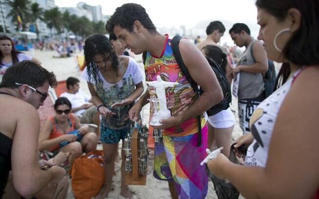 Vendedor aproveita movimento de peregrinos na praia de Copacabana, no Rio, para vender lembranças católicas no domingo (21)