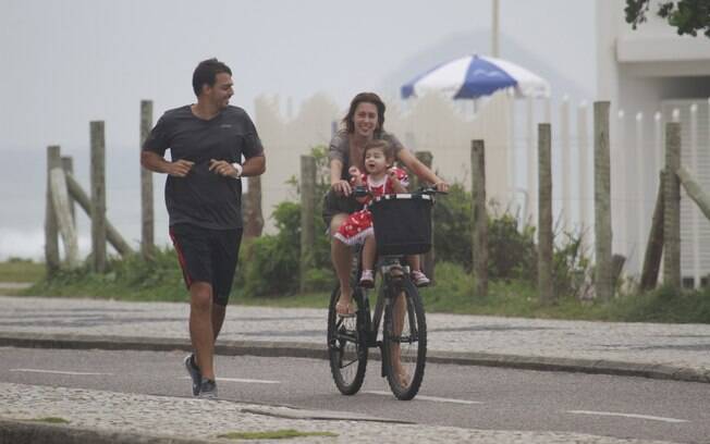 Dani Monteiro pedala com a filha, Maria, na orla enquanto o marido, Felipe Uchôa, corre