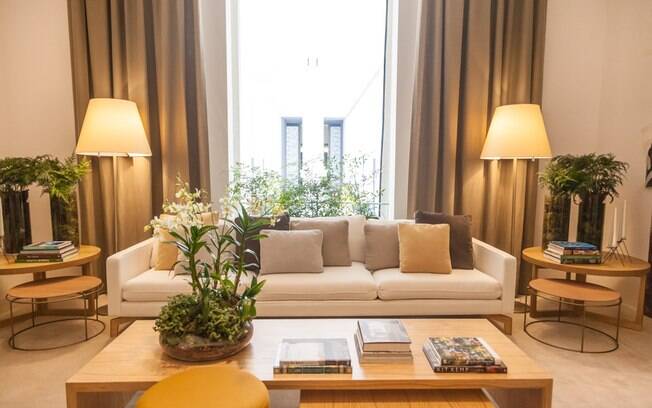 O arquiteto Bruno Gap criou um ambiente simétrico para a Casa Cor SP. Ao lado direito e esquerdo do sofá, encontra-se luminárias e mesas de apoio idênticas. As almofadas sobre ele também seguem divisão similar