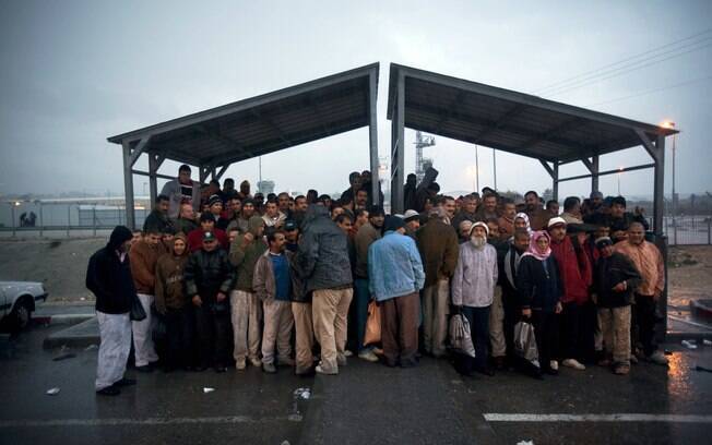 Trabalhadores palestinos se abrigam por causa da chuva enquanto esperam transporte depois de cruzar a fronteira para trabalhar em Israel (Arquivo)