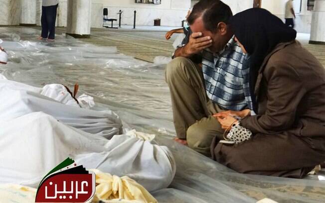 Homem e mulher velam corpos de sírios após suposto ataque com gás venenoso lançado pelas forças do regime de Assad