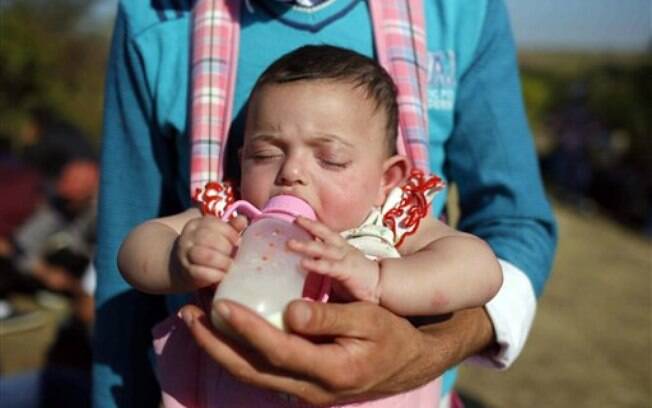Homem alimenta bebê enquanto imigrantes refugiados tentam chegar à Europa