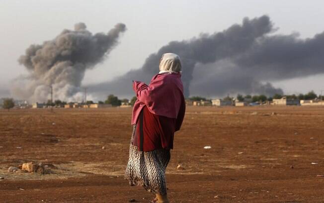 Mulher observa coluna de fumaça após um ataque aéreo em cidade da Síria em 2014, também contra o Estado Islâmico
