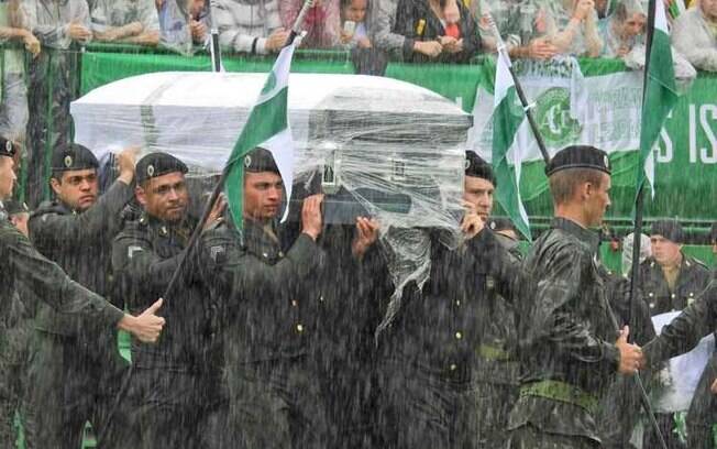 Sargentos do Exército Brasileiro carregam os corpos das vítimas da tragédia da Chapecoense, rodeados pela bandeira do clube