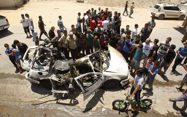 Palestinos se reúnem ao redor de destroços de carro que, segundo a polícia, foi alvo de ataque de Israel no norte da Faixa de Gaza (10/7)