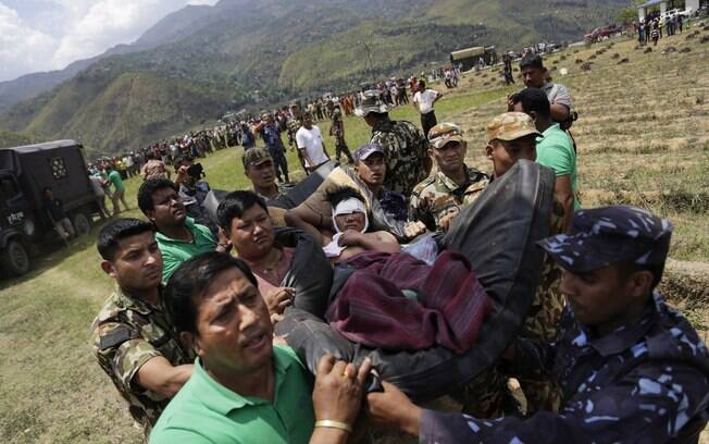 Soldados nepaleses transportam ferido em maca improvisada para helicóptero da força aérea indiana