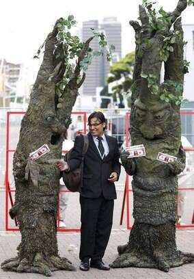 Manifestantes do Greenpeace fantasiados do árvores simulam entregar dinheiro a negociador