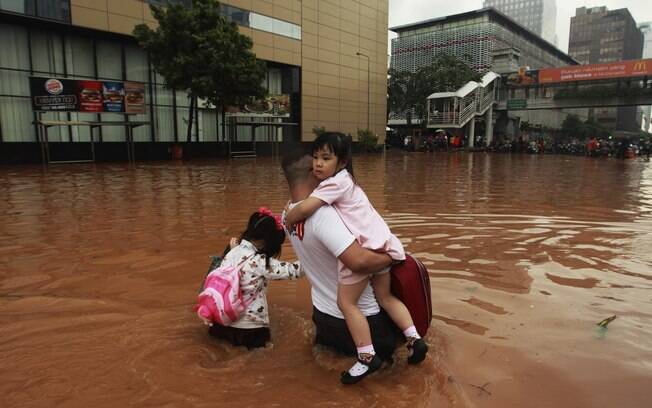 Pai atravessa com filhas rua inundada em distrito comercial de Jacarta (17/01/2013). Foto: Reuters