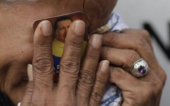 Venezuela chora segurando foto do presidente da Venezuela, Hugo Chávez, contra o rosto do lado de fora de hospital militar em Caracas (06/03)