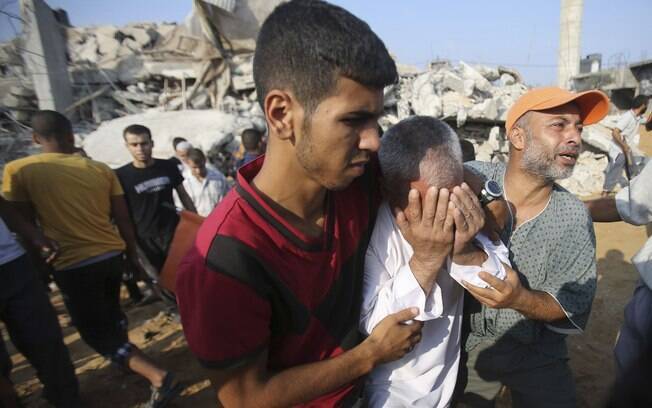 Palestino é amparado enquanto civis procuram por vítimas após casa ser destruída por ataque aéreo em Rafah, sul da Faixa de Gaza (29/07)