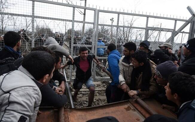 Refugiados quebram uma cerca de arame farpado na fronteira entre Grécia e Macedônia