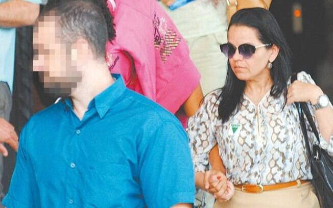 Jovem de 16 anos (com o rosto coberto) deixa delegacia após prestar depoimento sobre caso