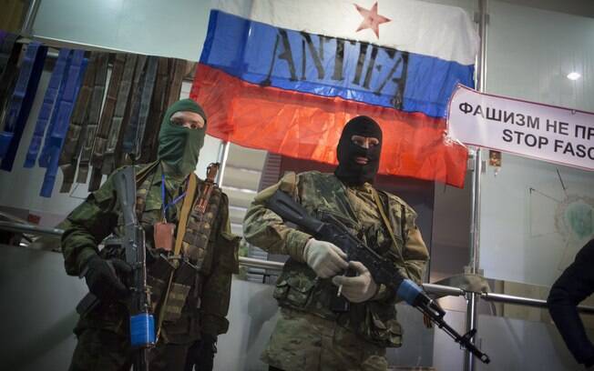 Atiradores mascarados pró-Rússia guardam entrada de escritório regional ucraniano do Serviço de Segurança em Luhansk com bandeira russa ao fundo (21/4)