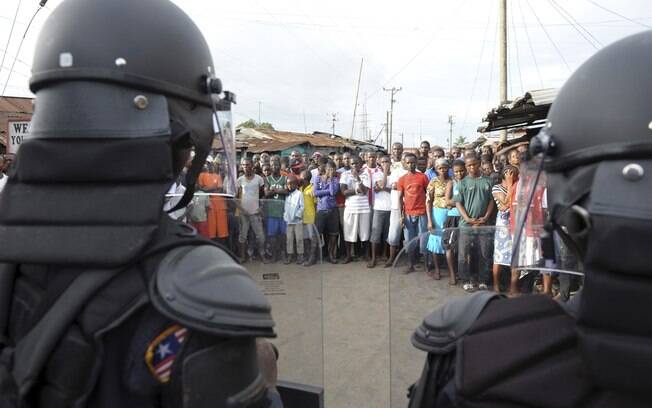 Policiais patrulham multidão para evitar que a área de quarentena do ebola imposta pelo governo seja ultrapassada