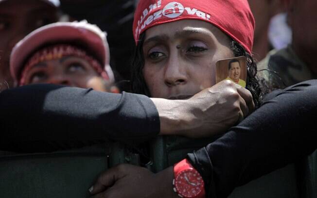 Mulher segura pequena foto de Hugo Chávez durante cortejo fúnebre do presidente venezuelano em Caracas (06/03)