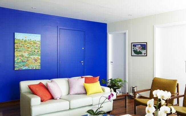 No apartamento decorado pelo estúdio Buji, a pintura da parede em tom de azul e a mudança da tapeçaria do sofá  transformaram o visual da sala  
