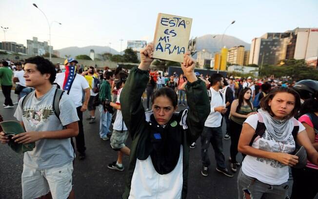 Jovem segura livro marcado em espanhol com a frase 'Esta é a minha arma' durante protesto contra repressão de estudantes em Caracas, Venezuela (13/2)