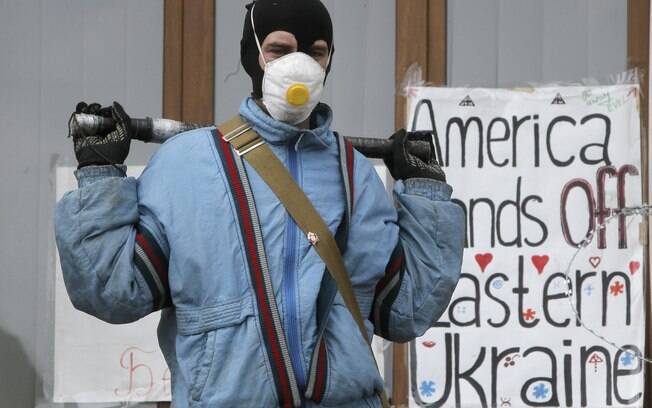 Ativista mascarado pró-Rússia guarda barricada em prédio da administração regional capturado em Donetsk. Cartaz diz: 'EUA, tirem as mãos do leste da Ucrânia' (19/4)
