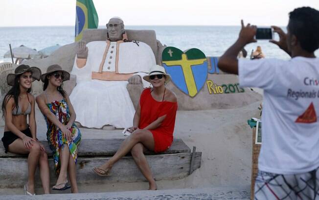 Turistas tiram foto em frente à imagem do papa Francisco esculpida na areia da praia de Copacabana, no Rio