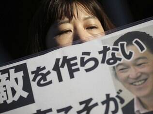 Uma mulher segura um cartaz com a foto de Kenji Goto com a frase