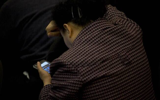 Parente de passageiros chineses de voo desaparecido da Malásia usa celular para assistir à coletiva sobre o caso em Pequim (17/3)
