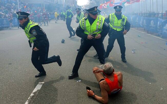Corredor de 78 anos é protegido por polícia após cair durante segunda explosão perto de linha de chegada da Maratona de Boston (15/04)