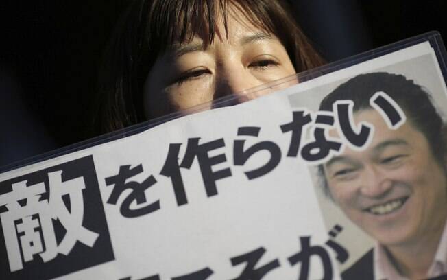 Uma mulher segura um cartaz com a foto de Kenji Goto com a frase 