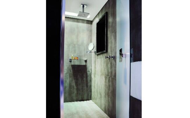 A sofisticação é levada até ao espaço de tomar banho, com chuveiro de teto e revestimento em porcelanto cinza, que foge dos azulejos normalmente utilizados