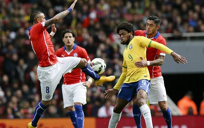 Luiz Adriano é cercado por chilenos enquanto tenta dominar a bola. Foto: AP Photo/Tim Ireland