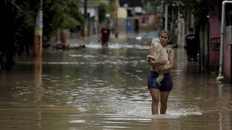 Mulher carrega um cachorro em meio a inundação no Rio de Janeiro 