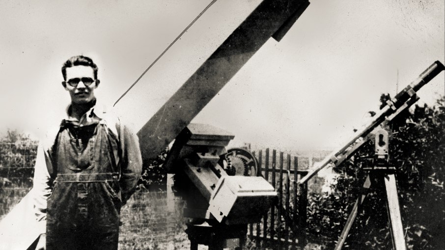Clyde W. Tombaugh, descobridor de Plutão, posa ao lado de telescópios que ele mesmo construiu em sua casa em Burdett, Kansas, antes de mudar a história da astronomia no Observatório Lowell.