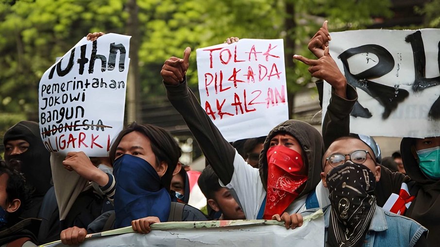 Manifestantes em Bandung, Indonésia, usam máscaras e seguram cartazes durante protesto, expressando críticas às políticas locais e reivindicando maior participação da população nas decisões