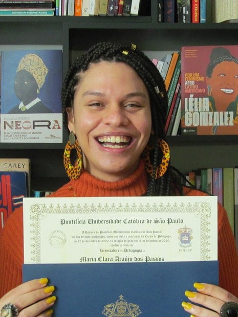 Maria Clara segura o certificado de conclusão de curso de pedagogia sorrindo 
