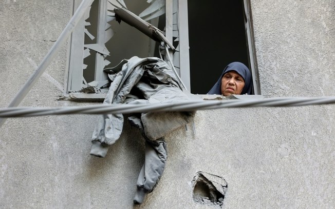 Uma mulher olha pela janela de um prédio atingido por um bombardeio israelense no bairro de Al Daraj, na cidade de Gaza, em 21 de maio de 2024