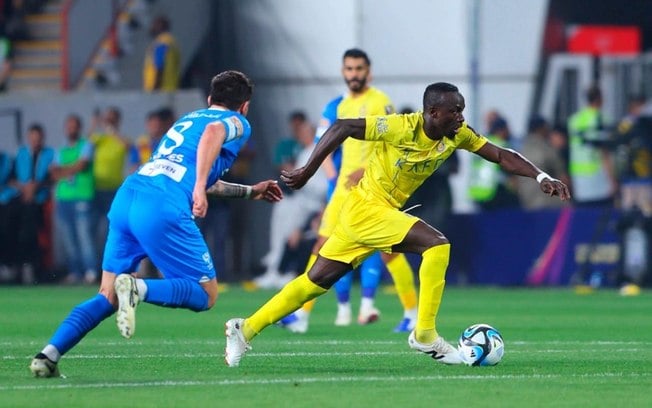 O craque senegalês Mané (de amarelo) dispara rumo ao ataque, tentando encaixar boa jogada para o Al Nassr. O português Rúben Neves tenta fazer a marcação -
