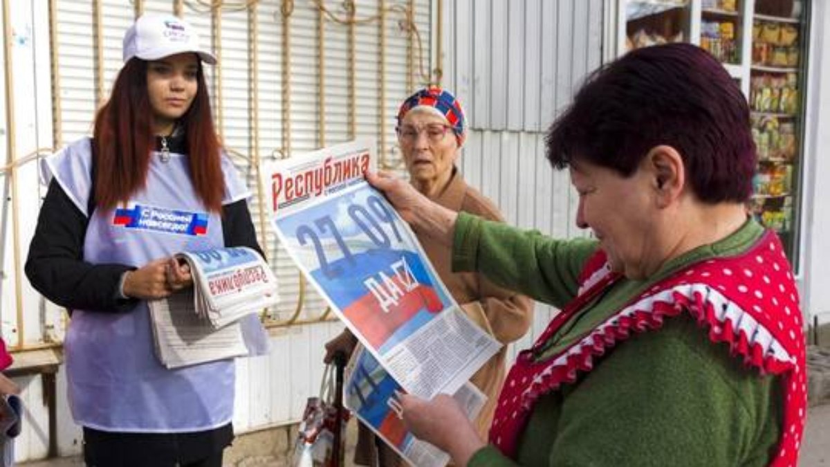 Voluntário da comissão eleitoral regional de Luhansk distribui jornais para cidadãos locais em Luhansk, 22 de setembro de 2022. No jornal lê-se em russo '27.09 Sim'