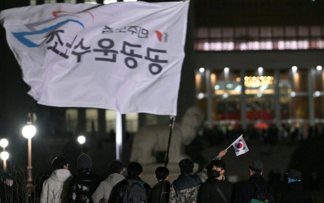 Homem tremula bandeira sul-coreana em frente à Assembleia Nacional em Seul, na Coreia do Sul, em 4 de dezembro de 2024