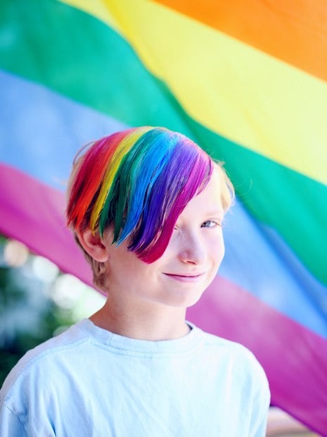 criança com cabelo colorido e bandeira LGBT ao fundo