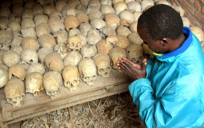 Sobrevivente ruandês reza sobre ossadas de vítimas do genocídio em uma vala comum em Nyamata, Ruanda