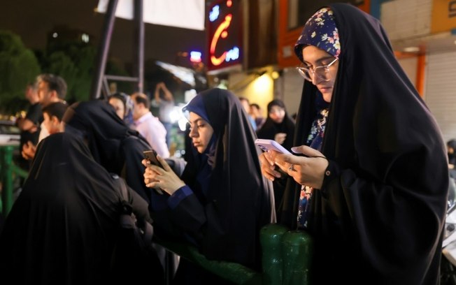 Iranianas acompanham pelo celular, em uma praça de Teerã, notícias sobre o desaparecimento do presidente do país