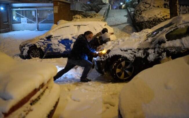 Pessoas empurram um carro preso na neve em Madrid