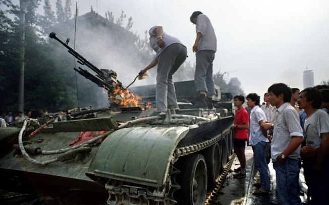 Chineses observam veículo blindado incendiado por manifestantes nos confrontos com militares perto da Praça Tiananmen (Paz Celestial) de Pequim, em 4 de junho de 1989