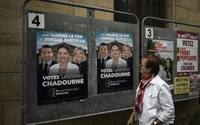 Mulher passa por alguns cartazes eleitorais das eleições legislativas francesas, em 2 de julho de 2024, em Libourne, sudoeste da França