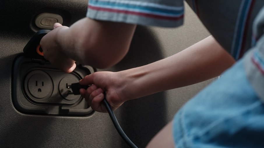 Protagonista do vídeo-publicidade da Rivian usa tomada do R1T para ligar aparelho eletrônico Protagonista do vídeo-publicidade da Rivian usa tomada do R1T para ligar aparelho eletrônico