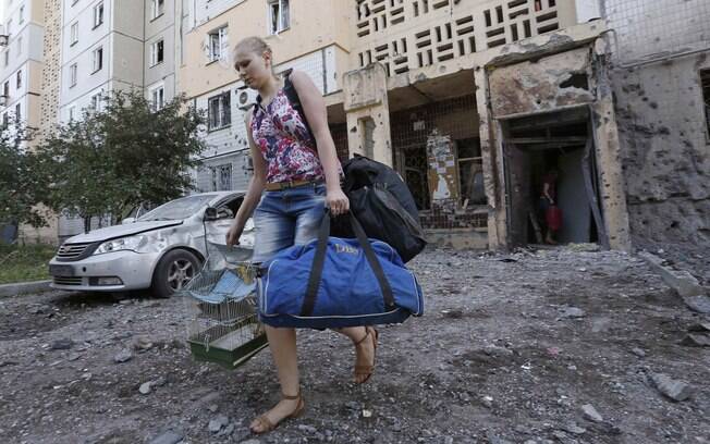 Mulher deixa prédio danificado por suposto bombardeio levando seus pertences na área central de Donetsk, Ucrânia (29/07). Foto: Reuters