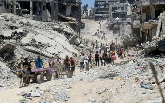 Palestinos caminham entre prédios destruídos no bairro de Shujaiya, na Cidade de Gaza