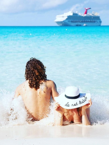 um homem de costas para o mar e uma mulher deitada com um chapéu branco na cabeça