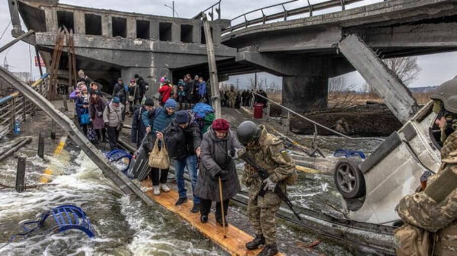 Pessoas são ajudadas por um soldado a passar por um rio através de uma ponte improvisada 